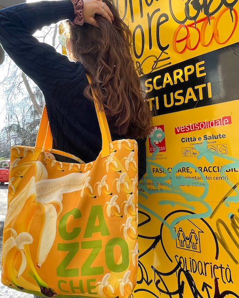The photo shows a shopping bag style bag that has "ca zzo che" and many bananas printed on it. You can buy this stylish bag design here in the "LA BELLA VITA club".  The main colours are yellow.